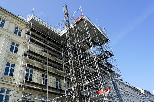 Repair of the facade of a historic tall house using scaffolding with temporary elevator, blue sky background