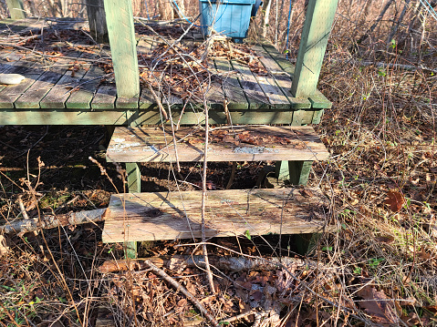 A set of old wooden stairs that are weathered and unsafe. Leaves cover the stairs.