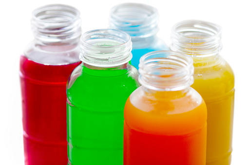 Multicolored energy drinks and fruit juices in opened bottles. White background.