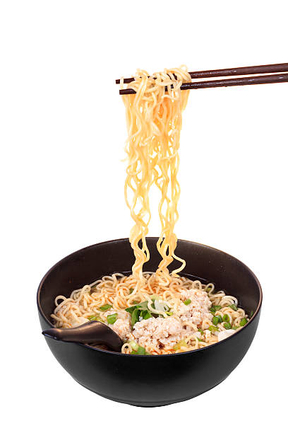 Chopsticks holding Asian noodles with minced pork above bowl stock photo