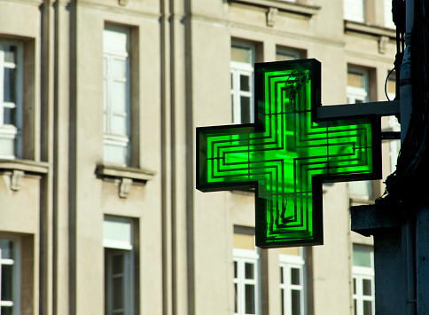 Pharmacy symbol, green cross city street, full frame view of tall buildings facades around. Lugo, Galicia, Spain.
