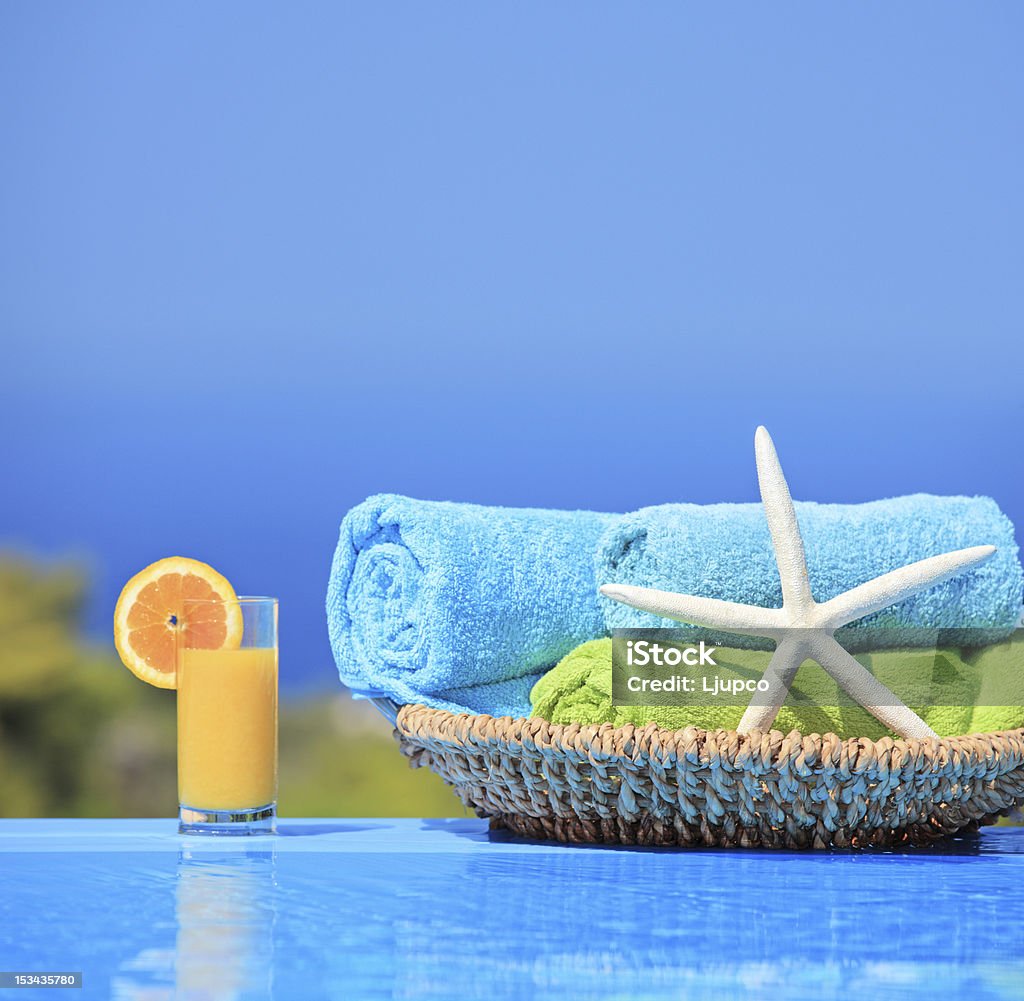 Orange juice, starfish and towels next to a pool Orange juice, starfish and rolled up towels next to a swimming pool Basket Stock Photo