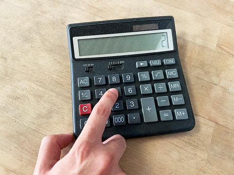 Using old and dusty calculator on the wood table. Accounting concept. Finger pushing calculator push button