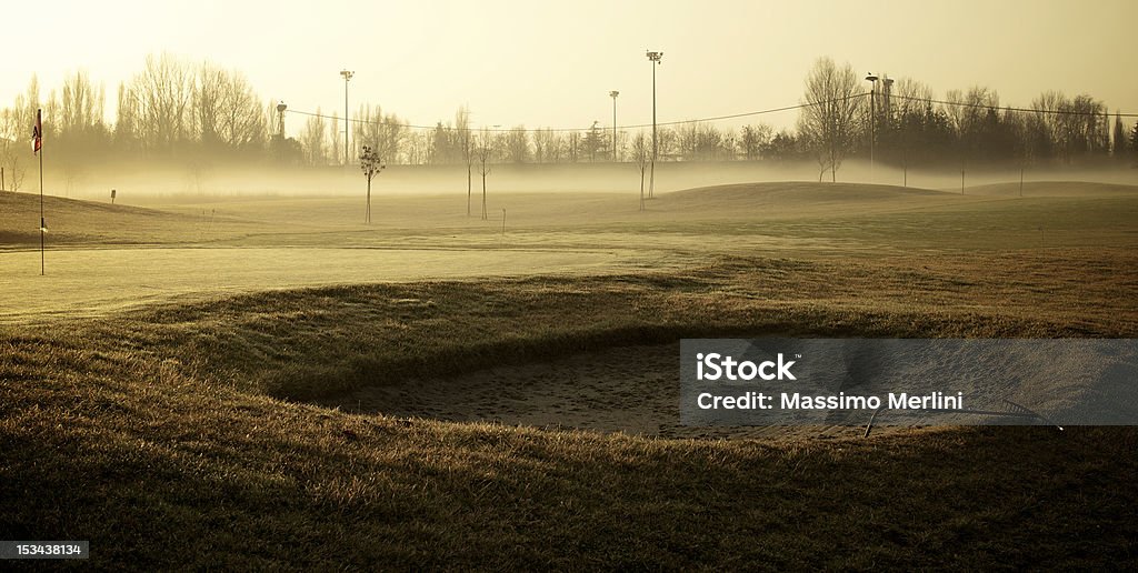 Golf Course in the foggy morning. The Morning fog settles the grass at the Golf Course as the sun rises in the background over the trees and rolling hills in the distance. The sand-trap in the foreground lays beneath the haze of the fog, and is hidden when observed from a distance. Copy Space Stock Photo