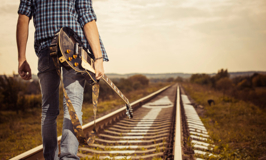 young man with guitar walking on a railroad to horizon