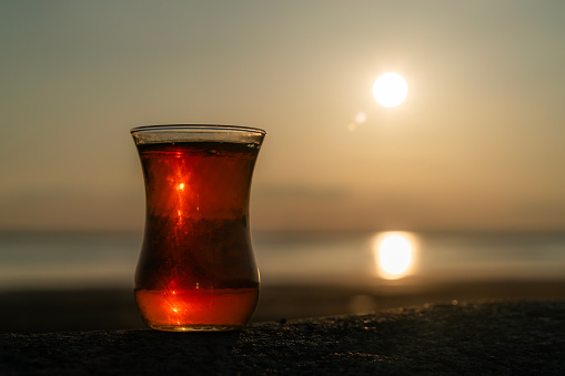 tea in glass cup and sunset view. Slender teacup. The sun is setting over the lake. Shot with a full-frame camera.