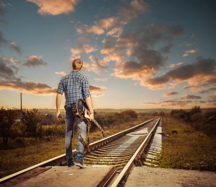young musician on a countryside railroad to horizon sunset