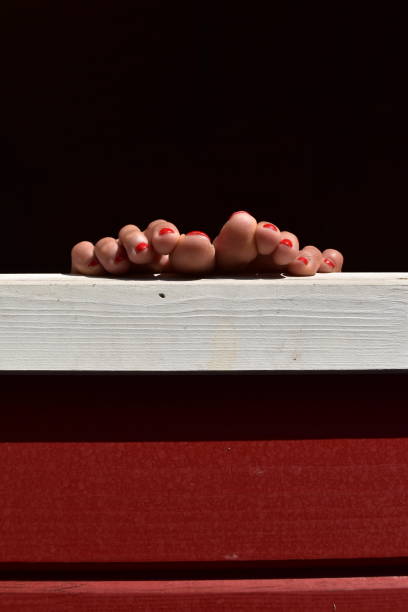 A female's feet with her nail polished in red, she is putting her feet up the window of a red and white painted wooden house