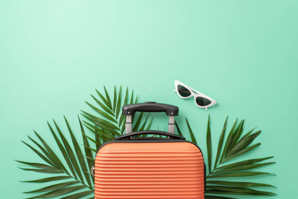 istock Immerse yourself in wanderlust with a captivating teal setting, featuring trendy orange suitcase, beach essentials, stylish sunglasses, palm leaves. Great for travel campaign ad 1534518803