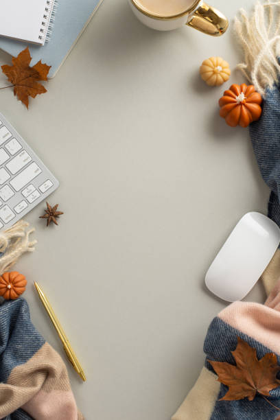 istock Autumn-inspired work essentials: bird's-eye top vertical view capturing notepad, gilded pen, keyboard, mouse, steaming coffee, cozy scarf and maple leaves on grey backdrop. Copyspace available for promotions 1534524785