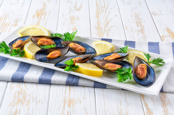 Cooked mussels with lemon and parsley on wooden table, selective focus. stock photo