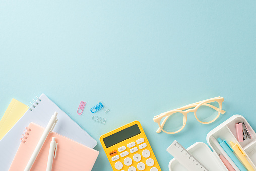 Embark on a successful educational journey with this top-down photograph of meticulously arranged school supplies and calculator on blue background. Use empty space to include text or advertisements