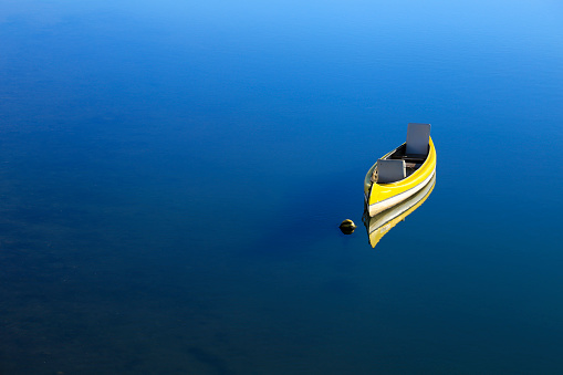 Beautiful Yellow canoe anchored on calm blue water.
