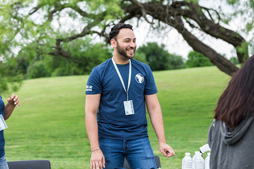 While standing at the sign in table, the mid adult man smiles at the unseen volunteers that are arriving to help clean up the park.