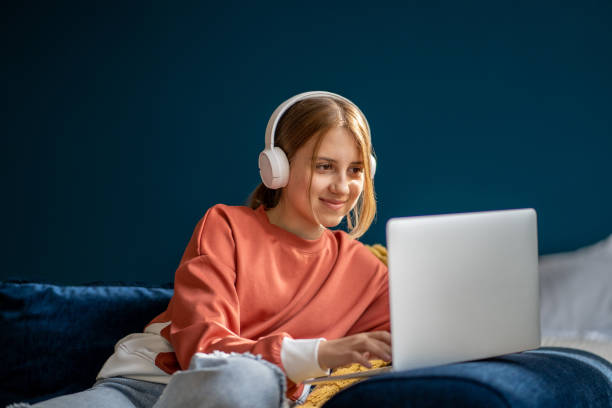 adolescente sonriente con auriculares escribiendo en una computadora portátil - sofa music teenager friendship fotografías e imágenes de stock