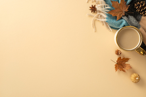 Welcome autumn with this picturesque scene: cup of fresh coffee, cozy plaid, small pumpkin candle, yellow maple leaves, pine cones and anise on pastel beige backdrop. Empty space for text or adverts