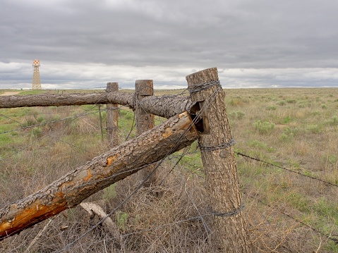 Barbed wire and log fence post at edge of Amache Internment camp and pasture land. The Granada national historic park was the site of Japanese internment during World War II. Cloudy skies and pasture at the edge of the park.