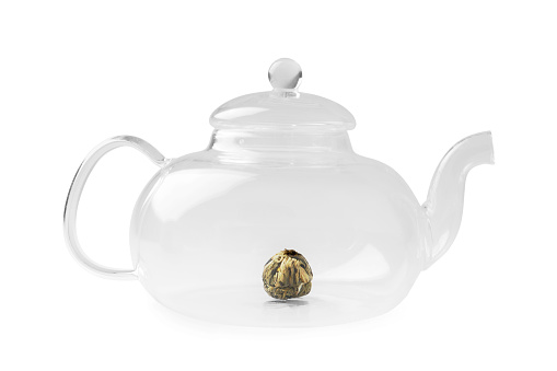 Empty glass transparent teapot and dry knitted flower green tea in it on a white background. Utensils for making tea.