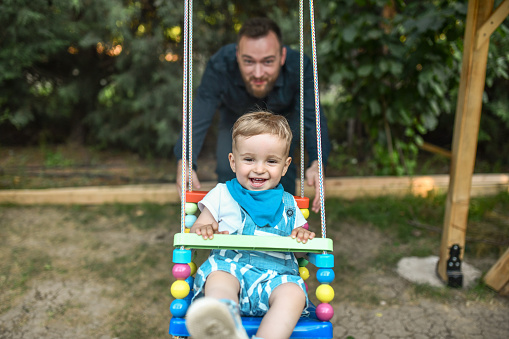 Excited Baby Boy Getting Rocked On Playground Swing By Father