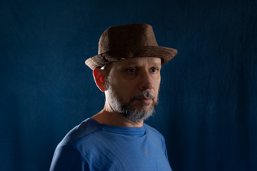 Portrait of bearded man wearing hat posing for photography. Isolated on blue background.
