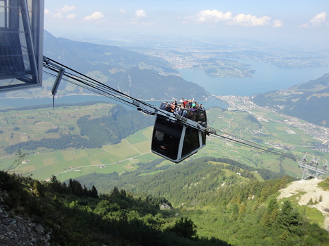 August 17, 2013: Mt. Stanserhorn, Lake Lucerne, Switzerland: A double-decker cable car -- the first open-air cable car in the world -- with riders both inside and on the top, ascending Mount Stanserhorn in Switzerland, with Lake Lucerne in the background.
