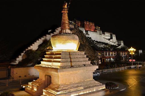 Beautiful night view of buddhist palace Potala in Lhasa, Tibet. White illuminated stupa on the foreground.