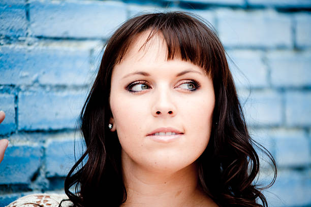Pretty girl face only looking off camera posed against blue painted brick wall