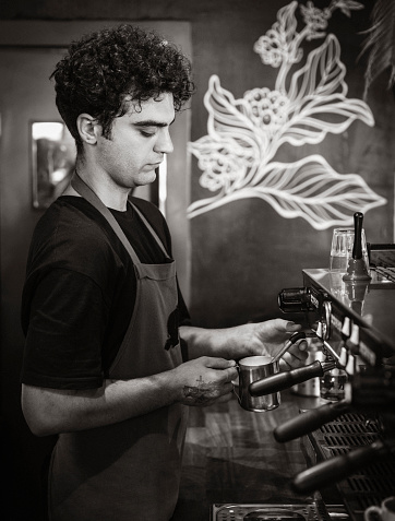 Side view of a male barista preparing cappuccino in a coffee shop