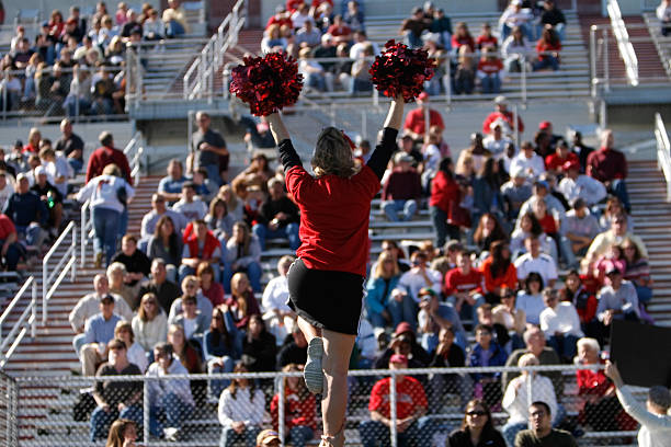 A football cheerleader is raised into the air infront of a large collegiate crowd.