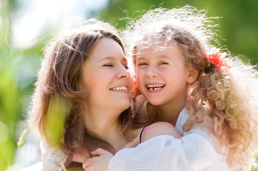 Little happy daughter and her young beautiful mother, both smiling. Nature background.