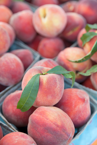 Cartons of fresh peaches with green leaves for sale at a farmer's market