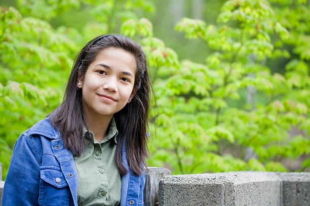 Preteen biracial asian girl outdoors with green trees in background stock photo