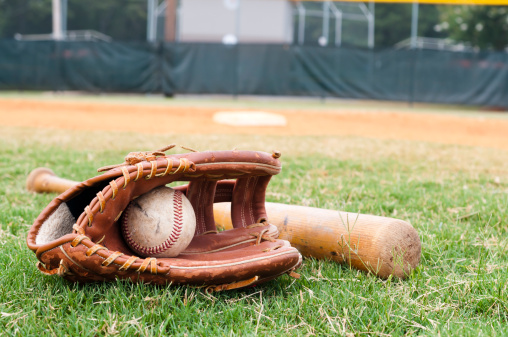 Old baseball, glove, and bat on field with base and outfield in background.