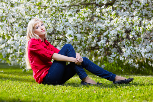 outdoor portrait of beautiful blonde girl posing on green grass near bloomin apple tree