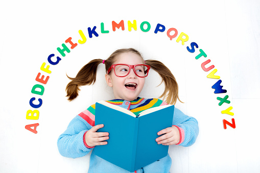 Happy preschool child learning to read and write playing with colorful roman alphabet letters. Educational abc toys and books for kids. School student doing homework. Kid reading in kindergarten.