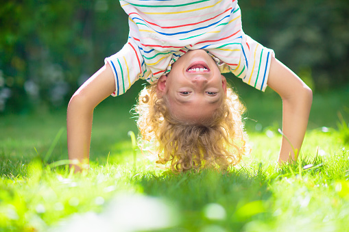 Little boy hanging upside down. Handstand exercise for little kids. Active child playing on sunny garden lawn. Summer fun. Kids play outdoor. Healthy sports activity in beautiful park.