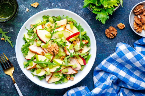 istock Waldorf salad with fresh apple, celery, lettuce, grilled chicken fillet, arugula and walnuts on plate, blue table background, top view 1534868332