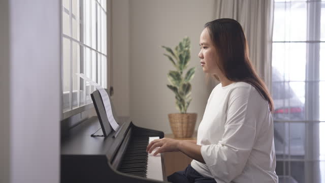 Asian woman enjoys playing piano at home. Musical instrument practicing and learning