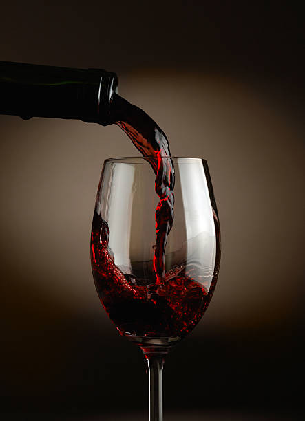 Red wine pouring in glass over dark background stock photo