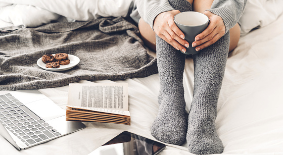 Young woman relaxing and drinking cup of hot coffee or tea  on a cold winter day in the bedroom