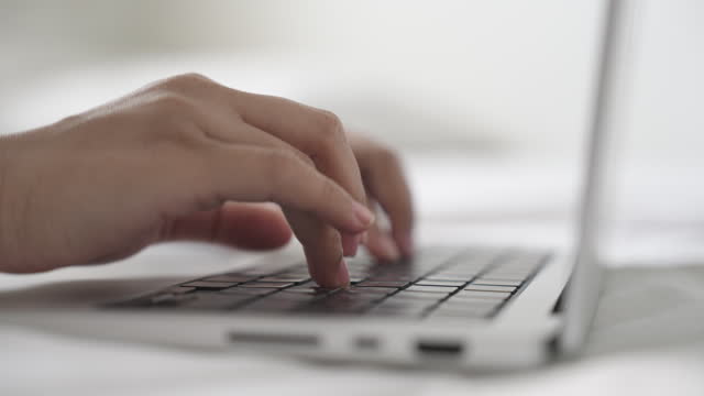 Close-up of hands typing on a laptop working on a bed