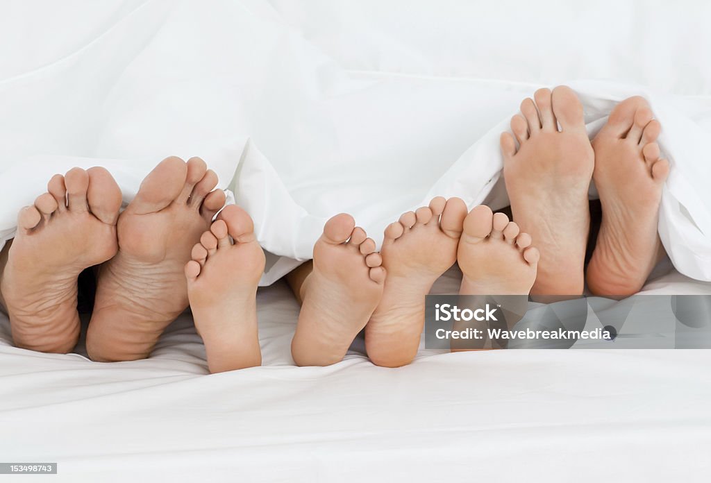 Familia en la cama en su casa con los pies que muestra - Foto de stock de Familia libre de derechos