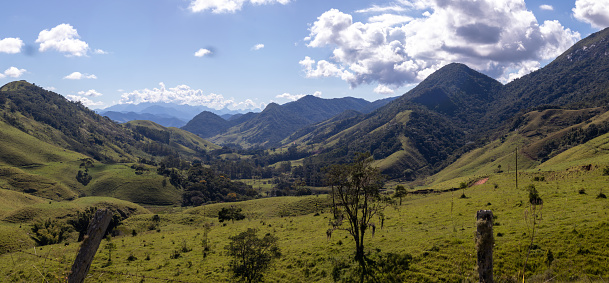 The photo shows rural Colombia at over 7000 feet above sea level, on the Andes Mountains, near the town of Choachi in the Cundinamarca department of the South American country. Rock strata can be seen on the side of the mountain. Clouds and sunlight make interesting shadows on the mountains. Cattle farming is an important occupation here.  Photo shot in the morning sunlight; horizontal format. No people.