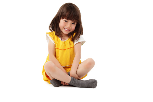 Cute little girl in a yellow dress sits on the floor and smiles for the camera. Horizontal shot. Isolated on white.