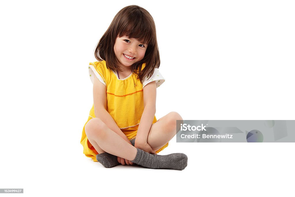 Young Girl Sitting With Crossed Legs - Isolated Cute little girl in a yellow dress sits on the floor and smiles for the camera. Horizontal shot. Isolated on white. Child Stock Photo