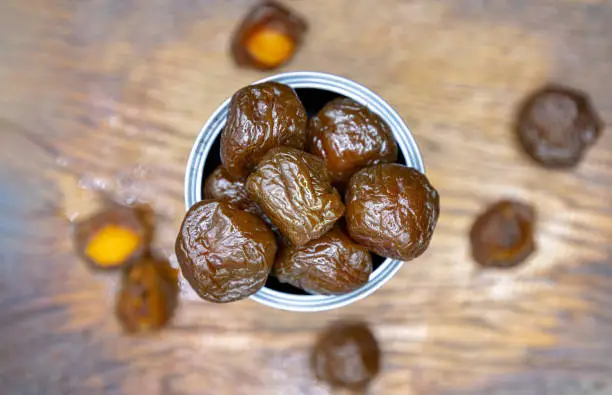 Flavored preserved chinese plums (Preserved fruits) in tin can on wooden background. Its flavour has sour, salty and sweet taste. Top view, Space for text, Selective Focus.