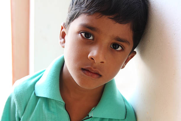 Young boy in turquoise shirt leaning his head against a wall stock photo