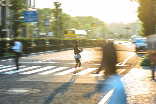 Mid adult Asian businesswoman crossing the street in the city. She is wearing black formal businesswear and a bag.