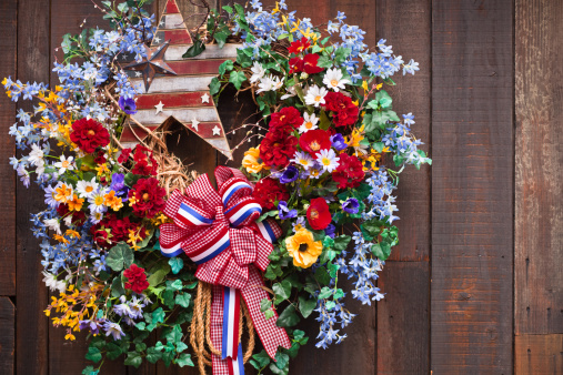 A close up of an Fouth of July wreath haning on a wood fence.
