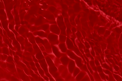 Redwater with ripples on the surface. Defocus blurred transparent red colored clear calm water surface texture with splashes and bubbles. Water waves with shining pattern texture background.